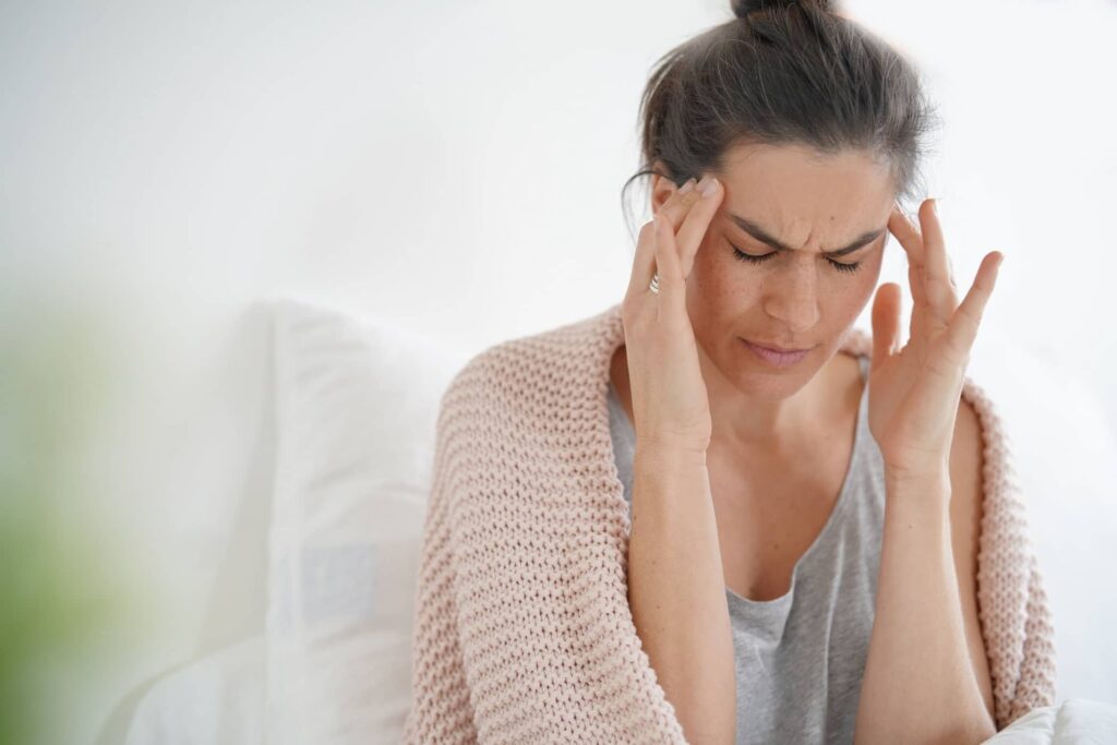 Woman touching her temples with eyes closed, appearing to experience a headache or migraine