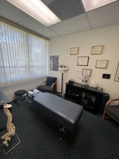 An adjusting room with a padded chiropractic table, a spine model and framed certificates