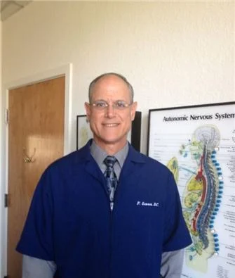 Dr. Francis Scorca in his navy clinic jacket, standing in front of a nervous-system wall chart