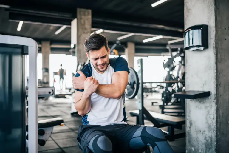 A man in a gym holding his sore shoulder