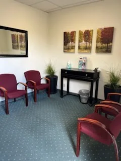 The waiting room with burgundy chairs and three tree paintings